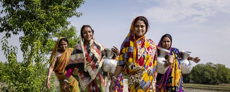 Brot für die Welt unterstützt Menschen bei der Anpassung an die Folgen des Klimawandels: In Bangladesch sind durch den Anstieg des Meeresspiegels Dämme gebrochen und Süßwasserteiche versalzen. Sauberes Trinkwasser ist kostbar. Der Brot-für-die-Welt-Partner CCDB Bangladesch arbeitet an Süßwassergewinnungs-Projekten und sorgt dafür, dass die Menschen in den durch den Anstieg des Meeresspiegels gefährdeten Regionen sauberes Trinkwasser erhalten.Foto: Frauen, wie hier Suparna Raptan (v.r.) aus der Umgebung von der Wasserstelle Vamia, tragen ihre Wasserkrüge, die sie an der CCDB Wasserstelle Vamia gefüllt haben, nach Hause.